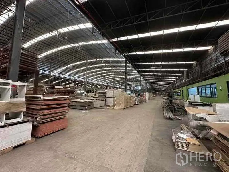 Factory for rent in Pathum Thani - Manufacturing area with stacked boards and materials under a high curved roof.