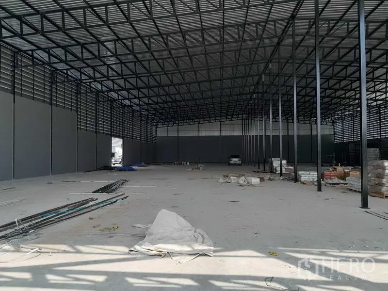 Warehouse for rent in Lam Luk Ka, Pathum Thani - Open-plan warehouse space with tall steel columns and materials stacked along the sides.