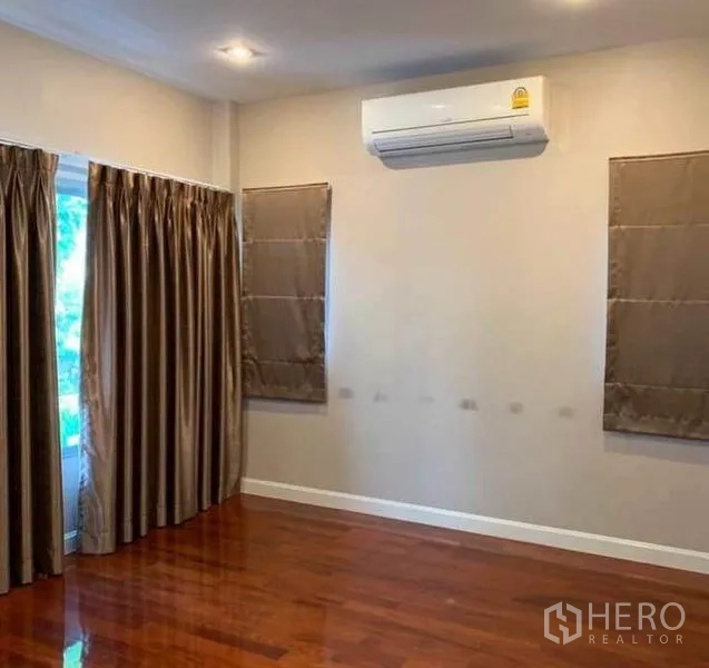 Detached House for sale in Mueang Pathum Thani, Pathum Thani - Spacious bedroom with hardwood flooring, draped windows and wall-mounted air conditioner.
