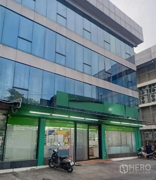 货栈 出租在Suan Luang, Bangkok - 四层蓝色玻璃外立面的商业仓库大楼，底层店面与前院停车区。