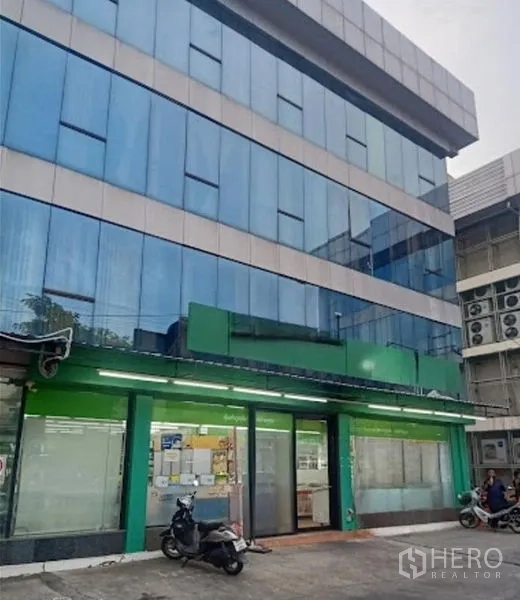 货栈 出租在Suan Luang, Bangkok - 四层蓝色玻璃外立面的商业仓库大楼，底层店面与前院停车区。