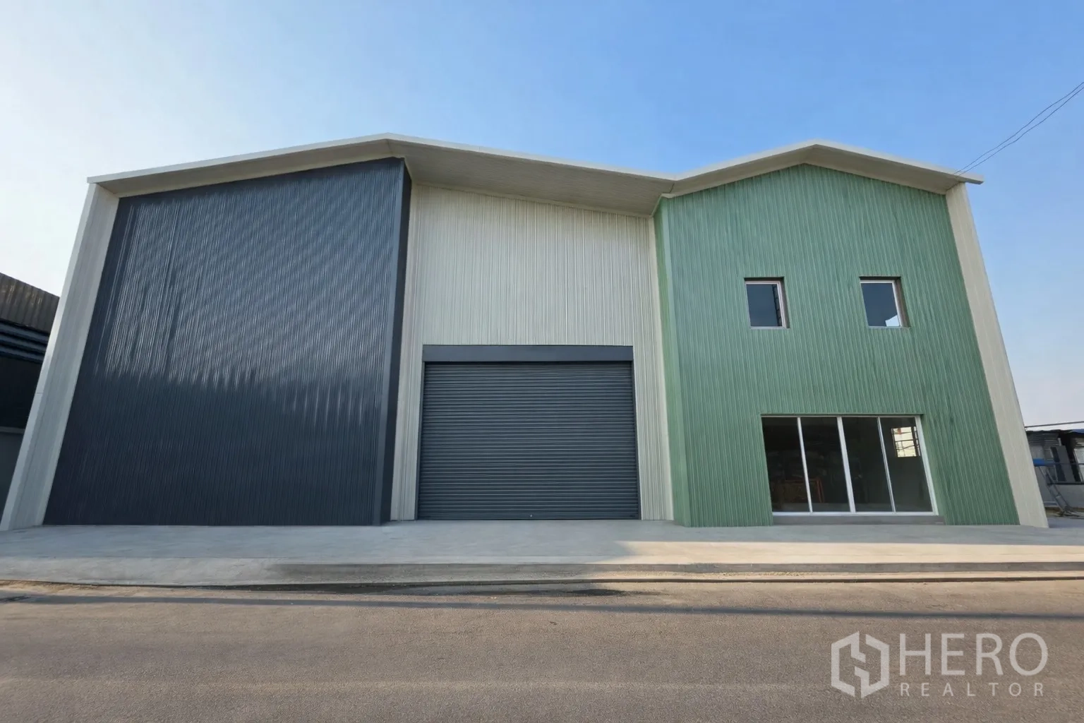 Warehouse for rent in Bang Kapi, Bangkok - Modern warehouse exterior with metal cladding, a large roller shutter and a glass-fronted office.
