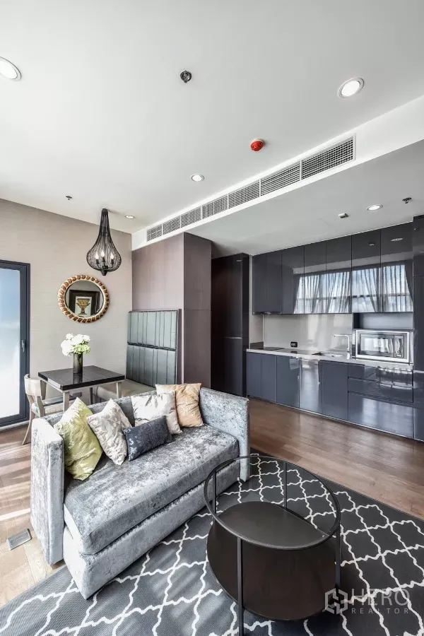 Condominium for rent or sale in Bang Rak, Bangkok - Open-plan living with plush sofa, dining nook, patterned rug, and glossy kitchen cabinetry.