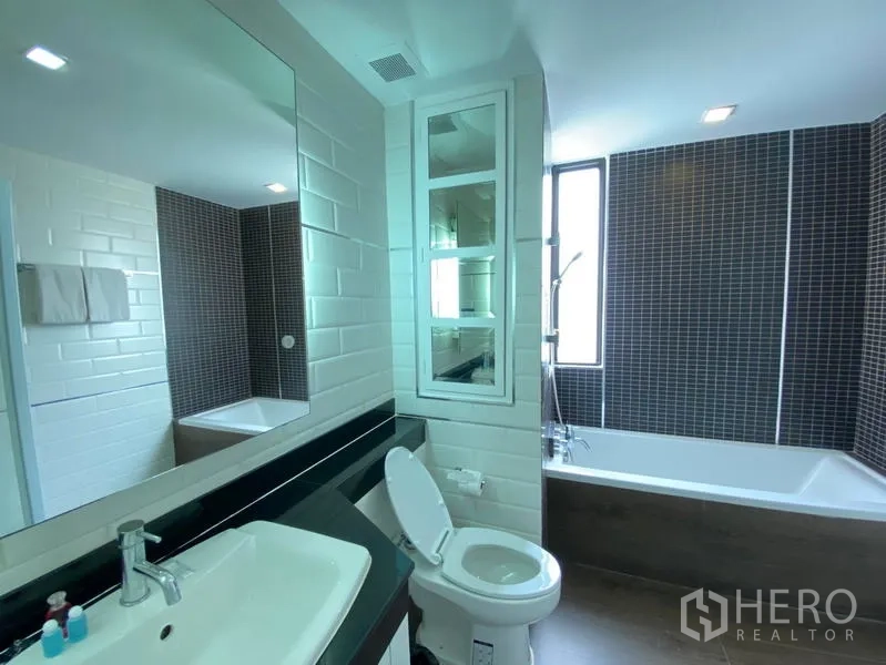 Condominium for rent in Khlong Toei, Bangkok - Bathroom with long vanity, bathtub with shower and contemporary tile finish.