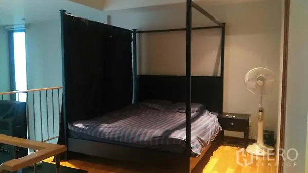 Condominium for sale in Khlong Toei, Bangkok - Cozy bedroom with four-poster bed, side table and wood flooring.