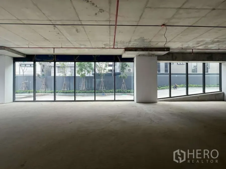 Retail Space for rent - Wide glass storefront on two sides with open-plan 77 sqm retail floor, columns and exposed services overlooking greenery.