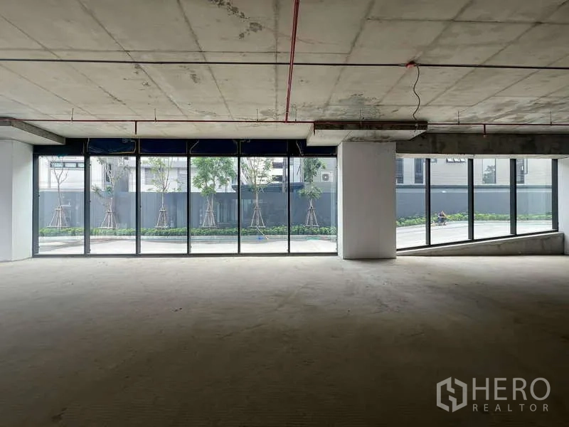 Retail Space for rent - Wide glass storefront on two sides with open-plan 77 sqm retail floor, columns and exposed services overlooking greenery.