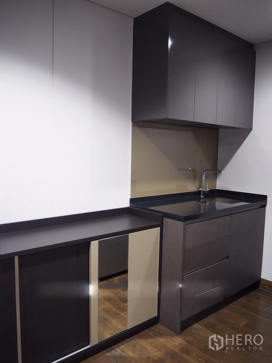Condominium for rent in Khlong Toei, Bangkok - Compact kitchenette with glossy cabinetry, black countertop and sink.