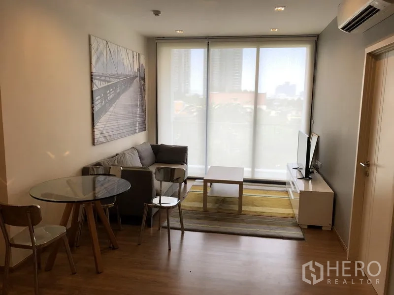 Condominium for rent in Watthana, Bangkok - Open living area with roller blinds, sofa, dining set and TV stand facing the balcony.