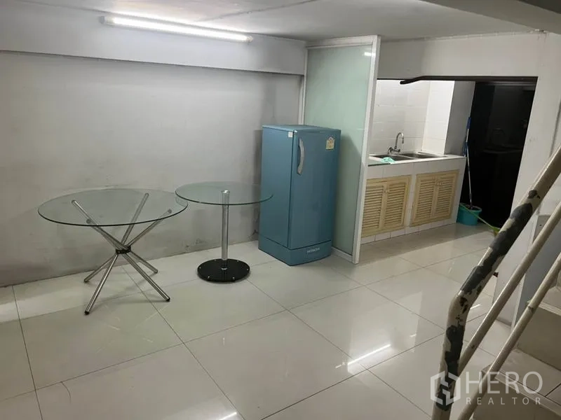 Shophouse for rent in Bang Rak, Bangkok - Mezzanine pantry with sink, blue refrigerator and glass tables on glossy tiles.