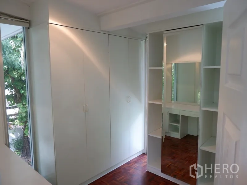 Detached House for rent in Khlong Toei, Bangkok - Walk-in closet with full-height wardrobes, mirror and parquet flooring.