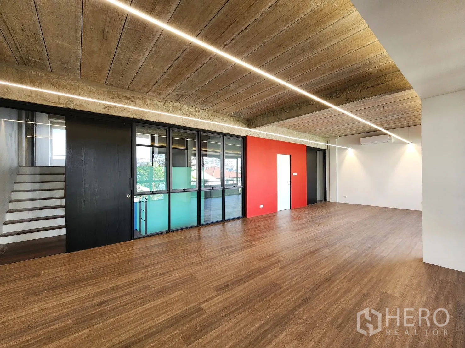 Home Office for rent in Chatuchak, Bangkok - Large workspace with wood flooring, red accent wall, and stair access behind glass.