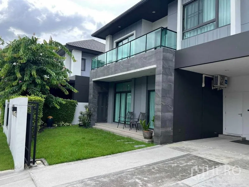 Detached House for sale in Khan Na Yao, Bangkok - Driveway and covered carport beside the house with upper-floor glass balcony and lawn.