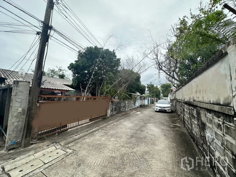 地 出售在Phra Khanong, Bangkok - 小巷视角显示地块大门、边界围墙以及远处停放车辆。