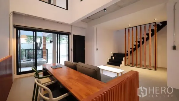 Townhouse for rent in Khlong Toei, Bangkok - Open-plan living room with wooden slat staircase and sliding doors leading to the terrace.