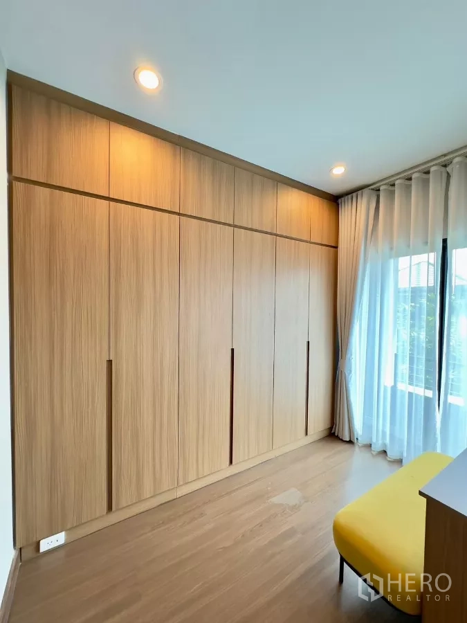 Detached House for rent in Samut Prakan - Wall of built-in wardrobes with warm lighting and wood floors.