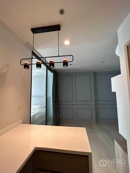 Condominium for sale in Pathum Wan, Bangkok - Kitchen peninsula with black pendant lighting facing a glass sliding door to the bedroom and paneled feature wall.