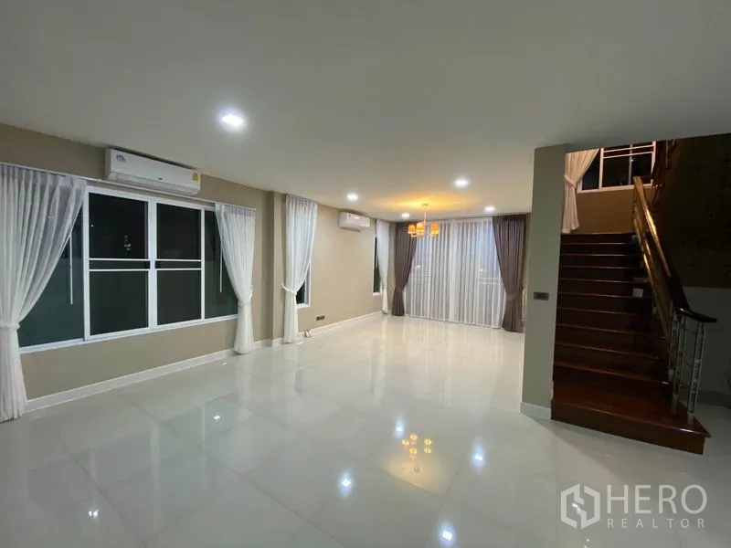 Detached House for rent in Prawet, Bangkok - Open-plan living and dining area with chandelier, large windows and wood staircase.