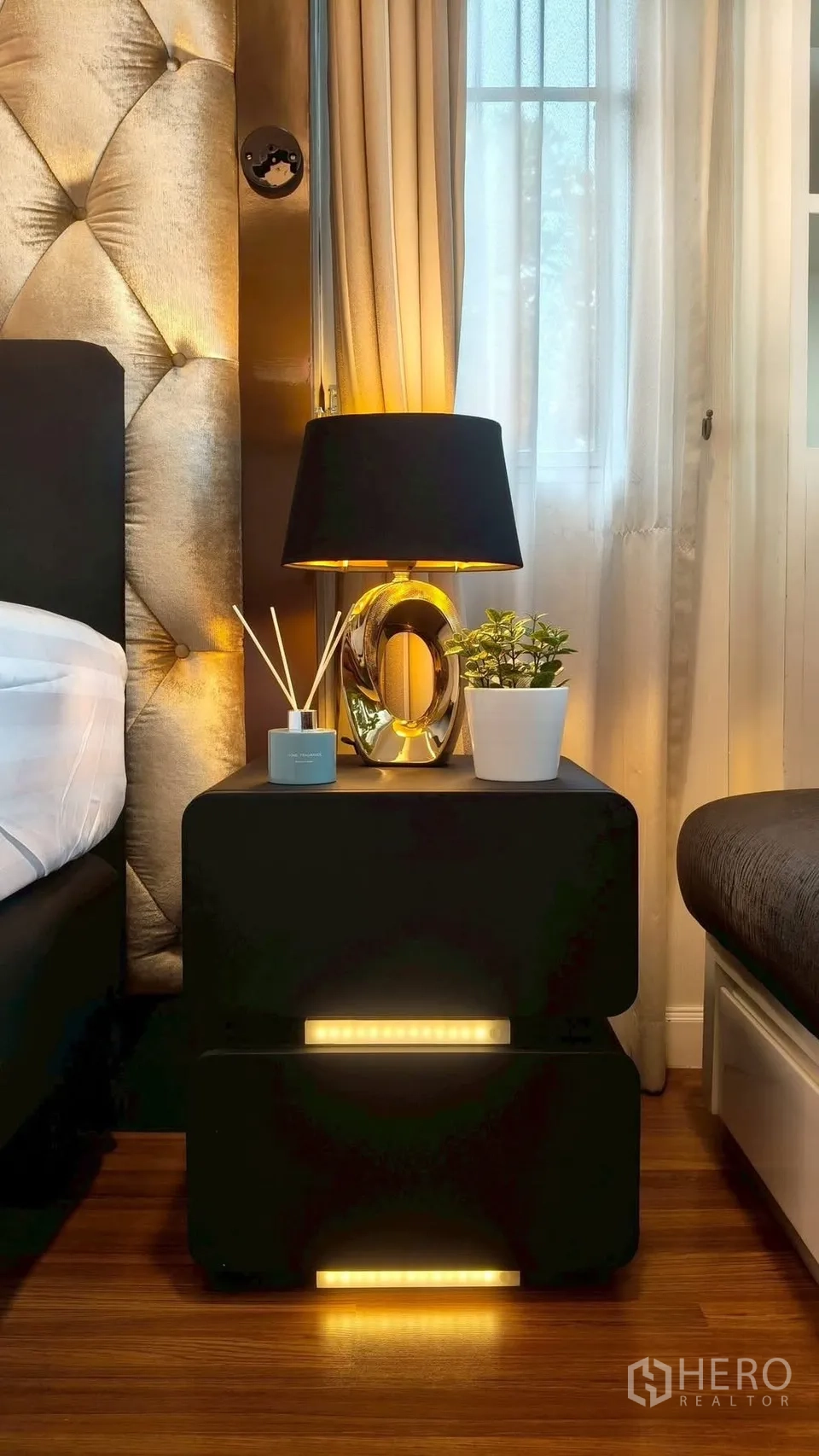 Detached House for rent or sale in Mueang Samut Prakan, Samut Prakan - Close-up of bedside table with contemporary lamp, plant and diffuser against a tufted headboard.