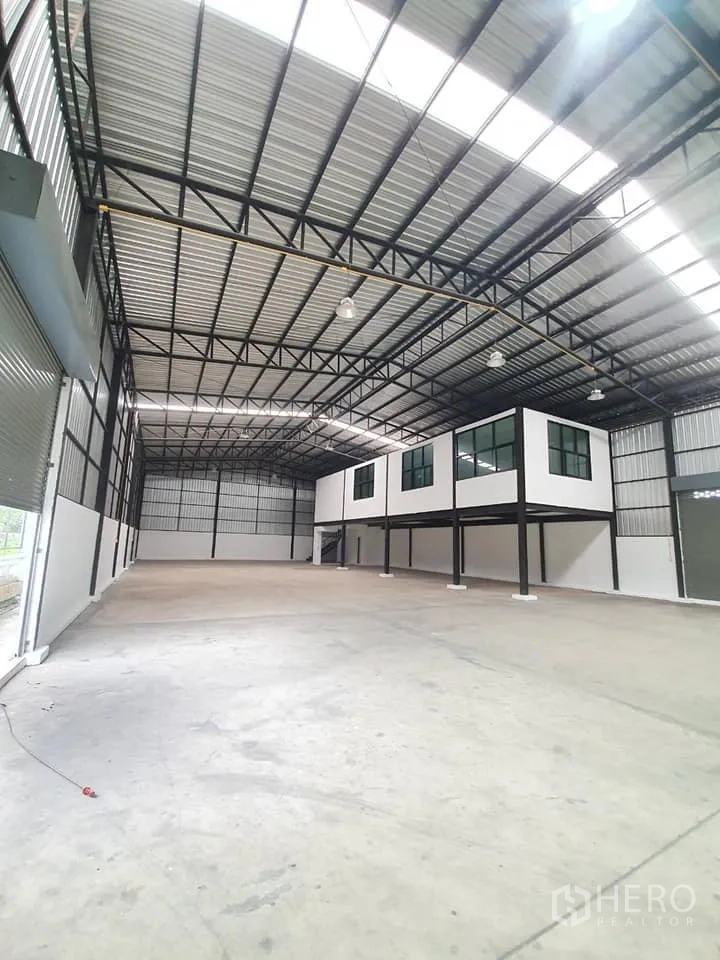 Warehouse for rent in Bang Khen, Bangkok - Interior side view with large roller door, high roof and raised mezzanine office structure.