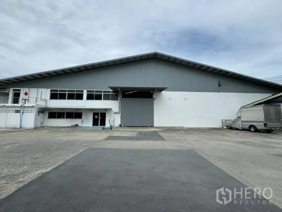 Warehouse for rent in Mueang Pathum Thani, Pathum Thani - Front view of a large warehouse with a wide roller shutter door and spacious paved truck yard.