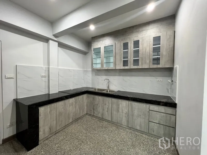 Home Office for rent in Watthana, Bangkok - Modern L-shaped kitchen with granite countertops and upper glass cabinets.