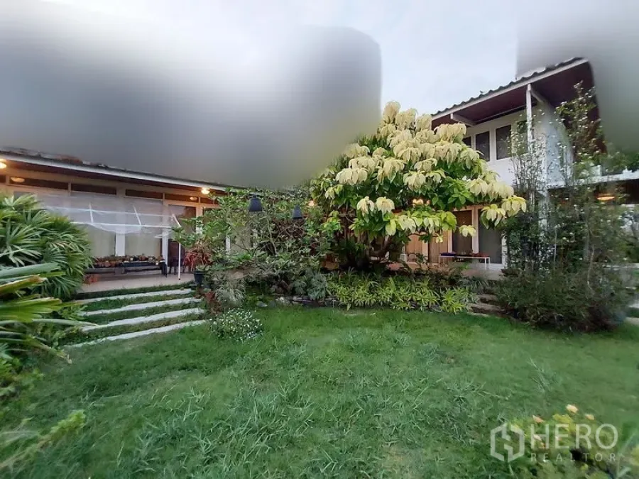 Detached House for rent in Mueang Samut Prakan, Samut Prakan - Front garden lawn and the home’s facade at dusk, framed by mature trees.