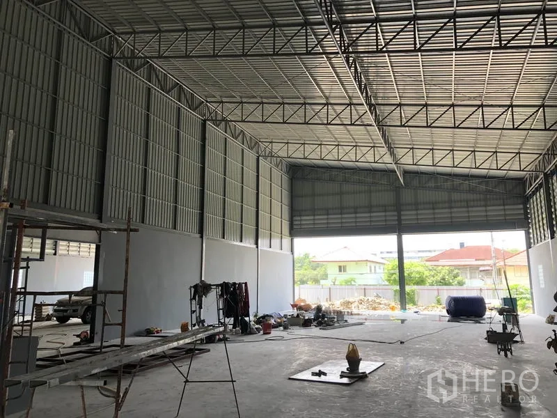 Warehouse for rent in Bang Khen, Nonthaburi - Warehouse interior facing a large roller shutter opening to the yard with natural light.