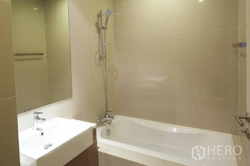 Condominium for rent in Bangkok - Beige-tiled bathroom with bathtub-shower combo and square basin vanity.