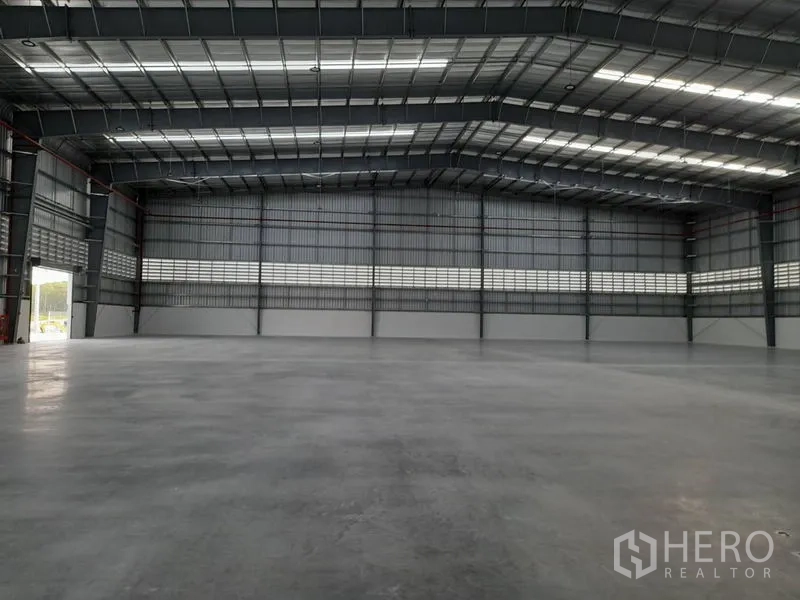 Factory for rent in Mueang Rayong, Rayong - Warehouse interior with high roller door, skylights, and smooth concrete slab.