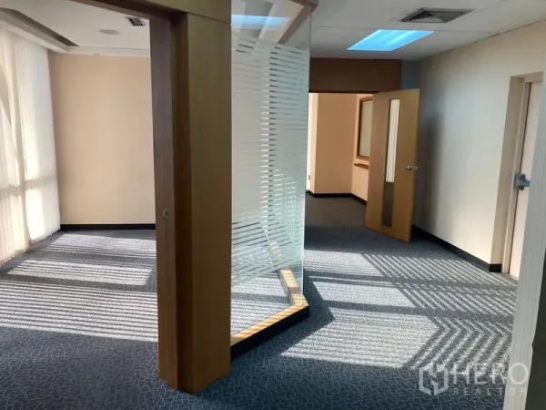 Office Space for rent - Bright circulation area with curved glass partition, open doors and natural light across patterned carpet.