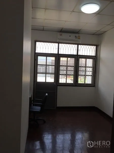 Townhouse for rent in Phra Khanong, Bangkok - Compact room with window grilles and door opening to a small balcony.