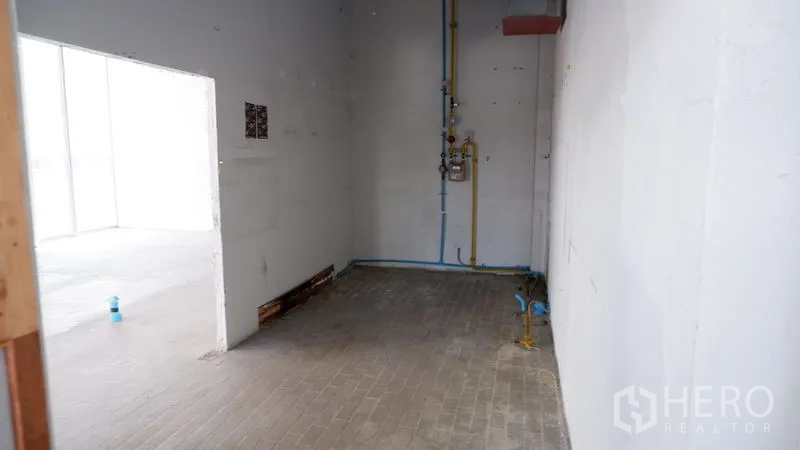 Retail Space for rent in Watthana, Bangkok - Back-of-house utility zone with white walls, exposed plumbing lines, and doorway to the main retail space.