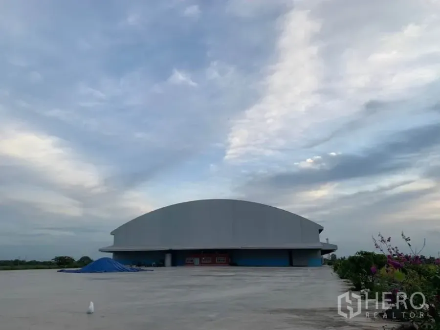 Warehouse for rent in Sai Noi, Nonthaburi - Expansive concrete yard and dome-roof warehouse exterior under blue sky in Sai Noi, Nonthaburi.