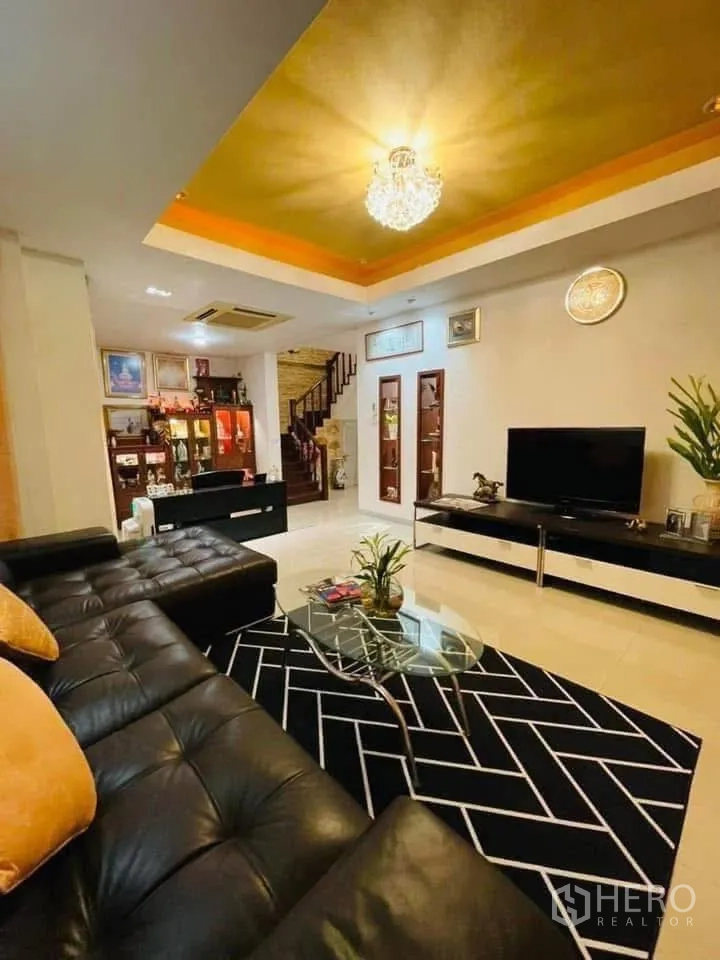 Detached House for rent or sale in Lam Luk Ka, Pathum Thani - Spacious living room with black leather sectional sofa, chandelier ceiling and TV unit.