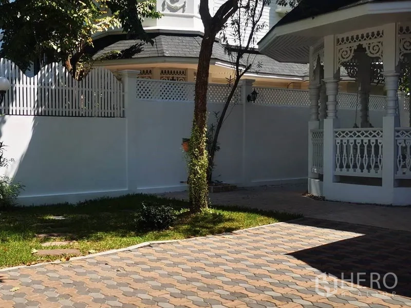 Detached House for rent in Mueang Samut Prakan, Samut Prakan - Paved driveway with a shaded gazebo and landscaped garden beside a white boundary wall.