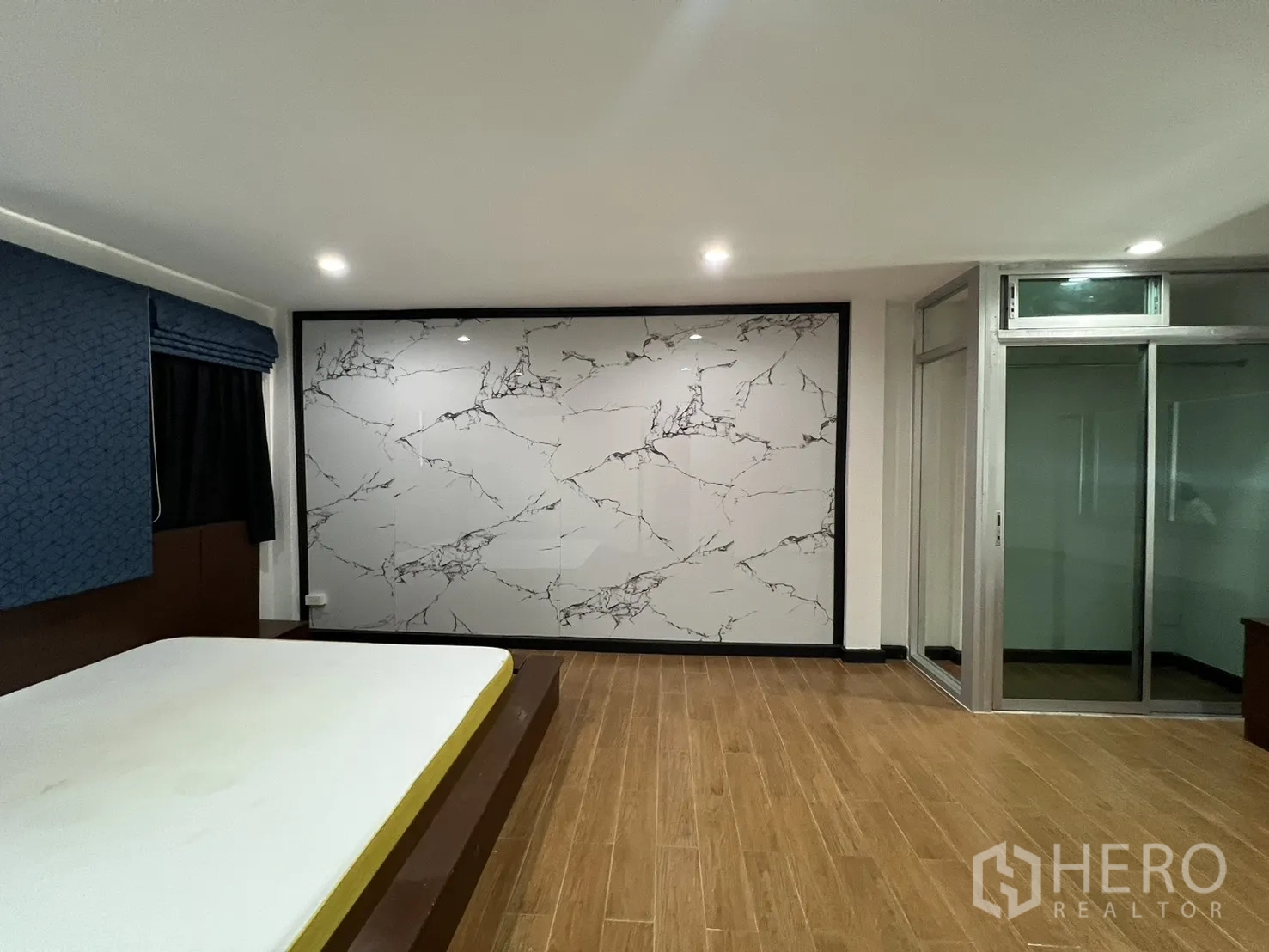 Townhouse for rent in Watthana, Bangkok - Spacious bedroom with wood flooring, marble feature wall and a glass partition.