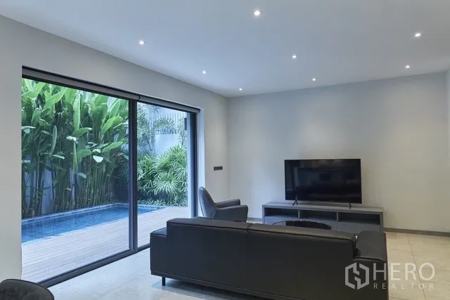 Townhouse for sale in Watthana, Bangkok - Media corner with sofa facing the TV and pool view through glass doors.