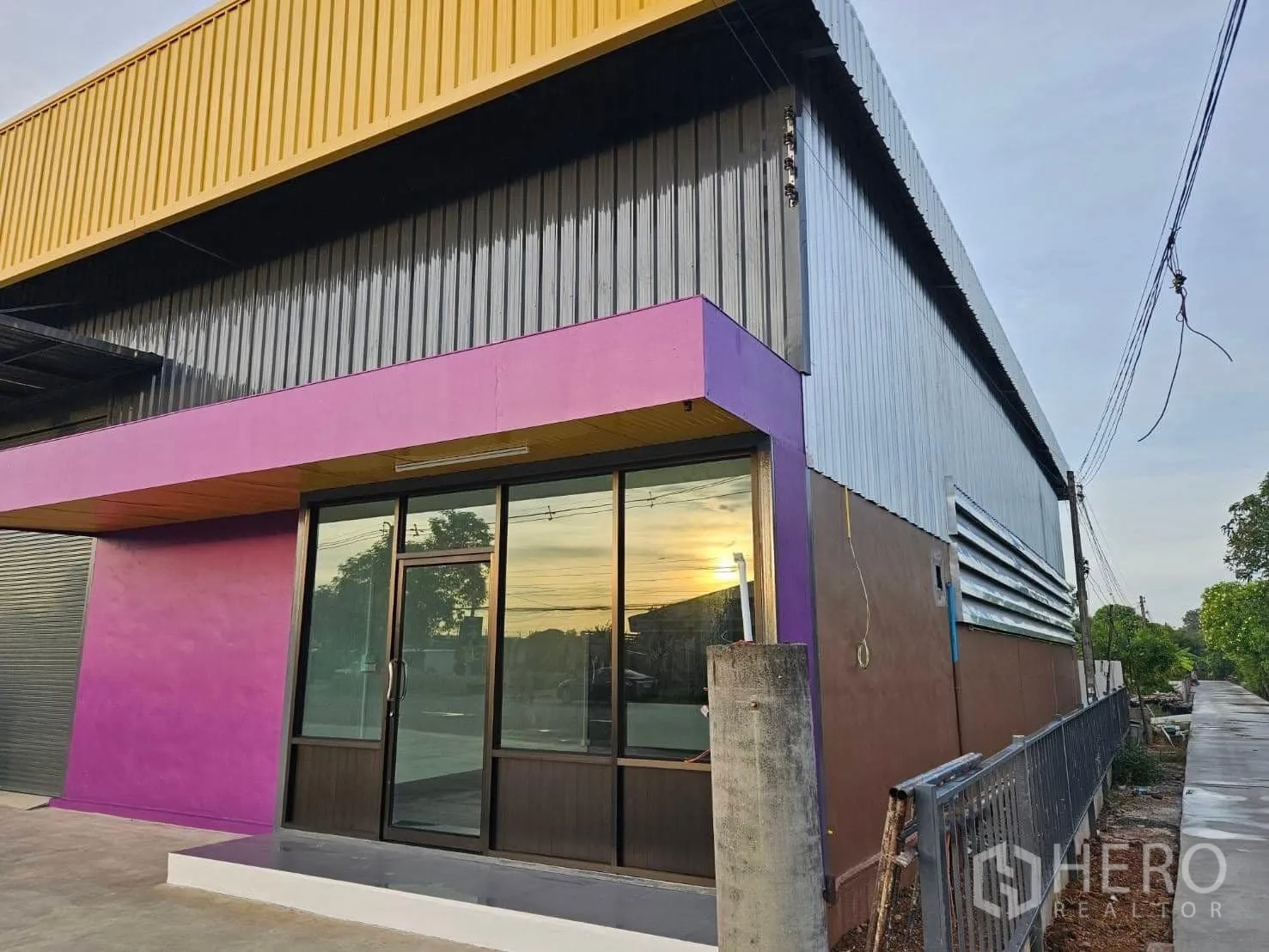 Warehouse for rent in Lam Luk Ka, Pathum Thani - Corner facade showing the glass-front office entrance with a purple accent beneath yellow roof panels.