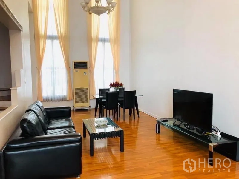 Townhouse for rent in Khlong Toei, Bangkok - Spacious living and dining room with high ceilings, leather sofa and TV console.