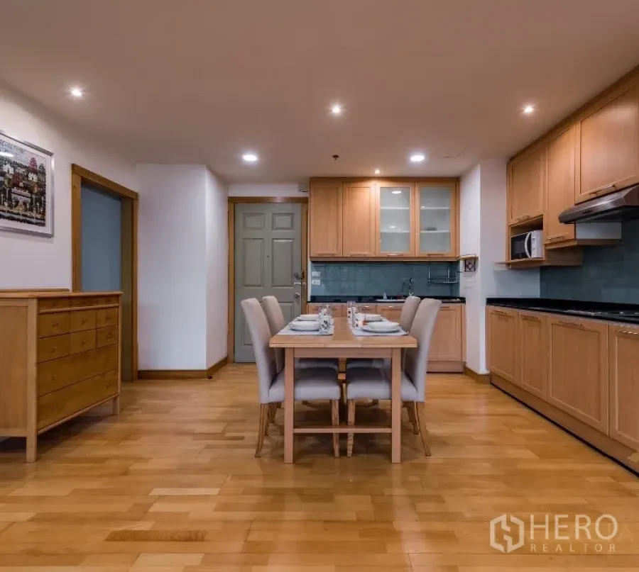 Condominium for rent or sale in Pathum Wan, Bangkok - Open-plan kitchen and dining area with wood cabinetry, four-seat table, and recessed lighting.