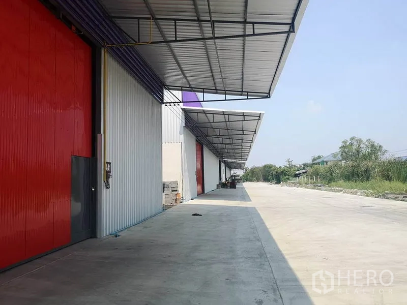 Warehouse for rent in Sai Mai, Bangkok - Covered loading bay with long canopy, red sliding doors and a wide driveway for truck access.