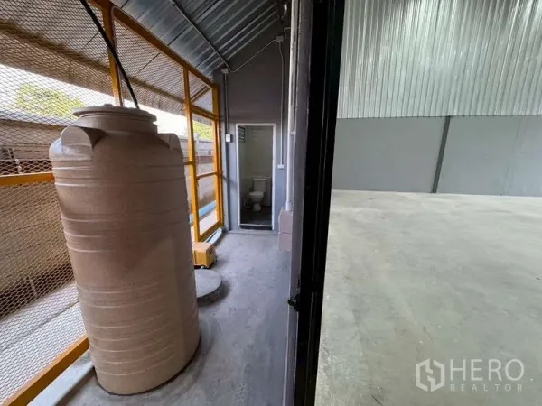 Warehouse for rent in Bang Phli, Samut Prakan - Service corridor with a water tank and mesh fencing beside the warehouse interior