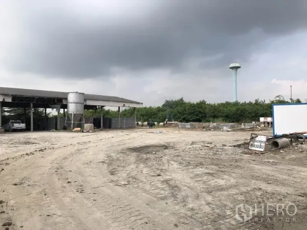 Factory for rent in Phra Nakhon Si Ayutthaya - Expansive work yard beside a covered shed, with a distant water tower and stockpiles.