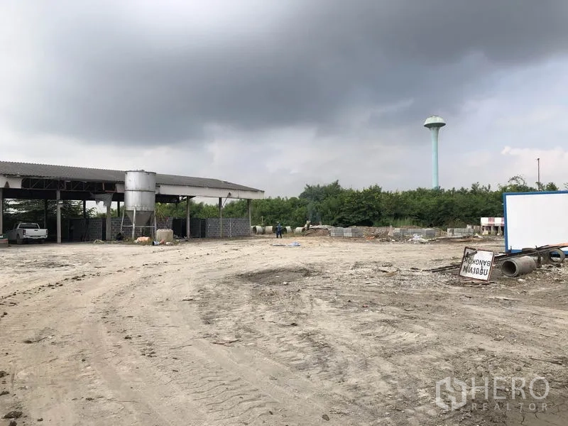 Factory for rent in Phra Nakhon Si Ayutthaya - Expansive work yard beside a covered shed, with a distant water tower and stockpiles.