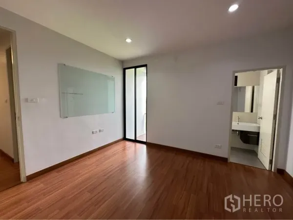 Townhouse for rent in Pak Kret, Nonthaburi - Bedroom with wood floors, glass door to balcony, and ensuite bathroom door.