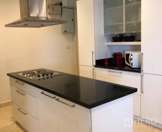 Condominium for sale in Khlong Toei, Bangkok - Modern white kitchen featuring a black granite island with gas hob and range hood.
