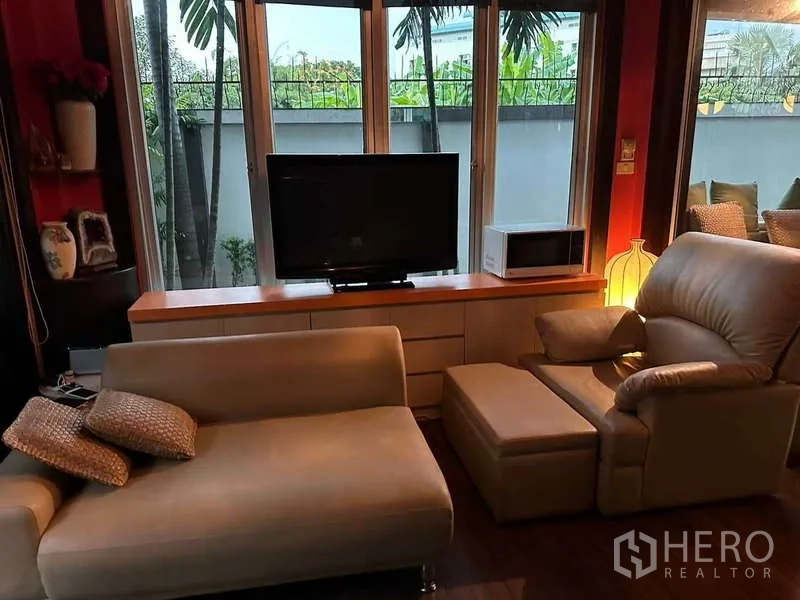 Detached House for sale in Suan Luang, Bangkok - Living area with TV console and sofa set by tall windows facing the garden.