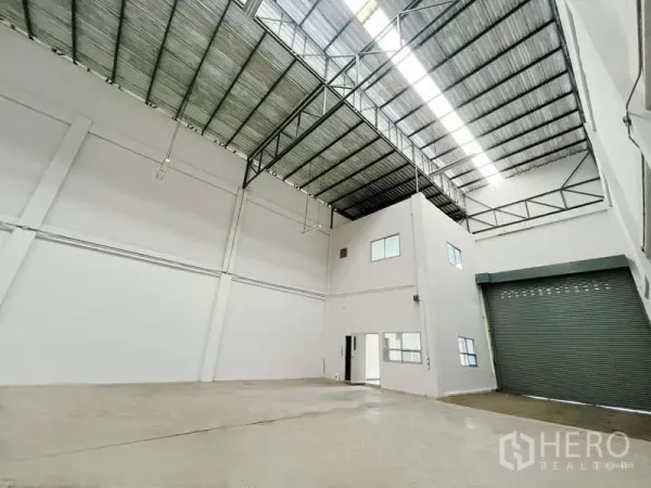 Factory for rent in Mueang Samut Sakhon, Samut Sakhon - Spacious high-ceiling factory interior with skylight, steel truss roof, and roller shutter beside an internal office block.