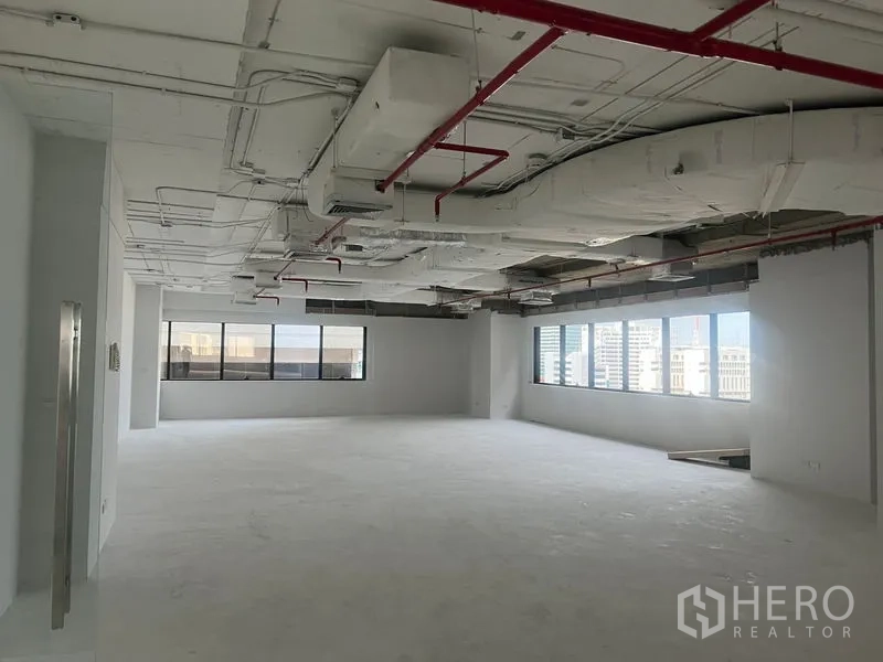 Office Space for rent - Spacious open-plan office interior with exposed ceiling ducts and red sprinkler pipes, large windows and city views.